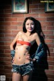 A woman in a red bikini top and denim shorts posing for a picture.