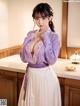 A woman in a purple shirt and white skirt posing in a kitchen.